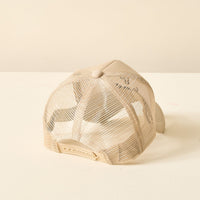 The Darling Effect's Tumbler Fan Club Trckr Hat is displayed from the back on a light surface, showcasing its adjustable strap and breathable beige mesh—ideal for fans of stylish, classic trucker hats.