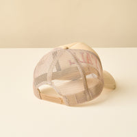 The Y'all Trucker Hat by the-darling-effect is displayed from the back on a light surface, showcasing its adjustable snapback and breathable beige mesh panels—perfect for fans of trendy hats.
