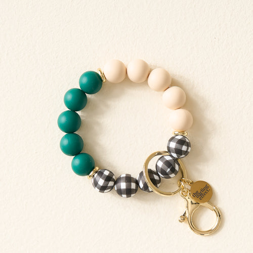 The Darling Effect Pretty in Plaid Hands-Free Keychain Wristlet features teal, cream, and black-and-white plaid silicone beads with gold key rings and a “she inspires others” charm, showcased on a light background.