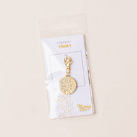The-darling-effect's February Jewelry Birth Flower Charm Gold features a gold charm engraved with a violet flower, attached to a clasp, and displayed on a "February violet" card in a clear plastic bag for personalized gifting.