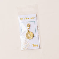 The-darling-effect's May Jewelry Birth Flower Charm Gold features an engraved lily of the valley and comes attached to a card with gold "darling effect" lettering, packaged in a clear plastic bag.