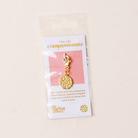 The-darling-effect Compassionate Jewelry Trait Charm Gold comes with a clasp, packaged on a card stating "You are compassionate" with the brand’s logo below, all inside a clear plastic sleeve.