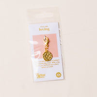 The-darling-effect’s Loving Jewelry Trait Charm Gold features a floral design on a card stating “You are loving.” Packaged in a clear plastic bag, it celebrates strength and selfless love with its heartfelt message.