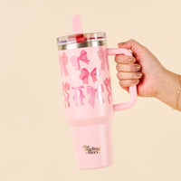 The-darling-effect Blushing Bows 40 oz Lifestyle Flip Straw Tumbler, featuring a pink bow pattern and leak-resistant flip straw lid, held in hand.