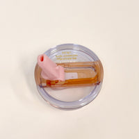 The Darling Effect 20 oz Peach Lifestyle Flip Straw Replacement Lid features a transparent circular design, a brown flip-top, pink silicone straw, and gold-printed text, shown on a plain white surface.