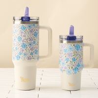 Two floral insulated mugs with handles and purple straws sit side by side on white tiles. The taller mug is the Secret Garden Blue 20 oz Lifestyle Flip Straw Tumbler by the-darling-effect, both with “the darling effect” at the bottom.