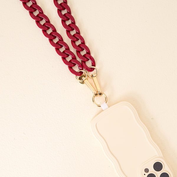 A cream phone case with wavy edges is paired with a chunky Burgundy Phone Chain from The Darling Effect, featuring gold clasps, on a light textured surface—an ideal accessory to elevate your game day look.