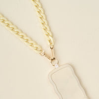 A close-up of The Darling Effect’s Cream Hold the Phone Crossbody Chain attached to a wavy-edged, light beige cardholder with gold clasps, set against a neutral background.