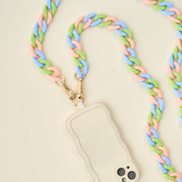 The Darling Effect Tri Lively Hold the Phone Crossbody Chain in pastel pink, green, and blue is paired with a beige wavy-edged phone case, creating a chic accessory set shown on a light cream surface.