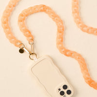The-darling-effect’s Marble Peach Hold the Phone Crossbody Chain pairs a cream phone case with wavy edges and a chunky peach strap, creating a stylish, on-the-go accessory shown on a light textured surface.