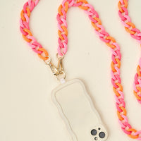 The Tri Sassy Hold the Phone Crossbody Chain by The Darling Effect features a white wavy-edged phone case paired with a chunky pink and orange chain strap with gold clasps, making it a chic accessory for any stylish outfit.