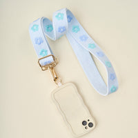 The Darling Effect's Blue Hold the Phone Crossbody Strap, paired with a wavy cream phone case, features turquoise and blue floral patterns—a stylish, hands-free accessory displayed on a light background.
