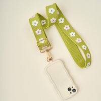 The Darling Effect's Green Hold the Phone Crossbody Strap, featuring a white and pink flower pattern, is attached to a cream phone case.