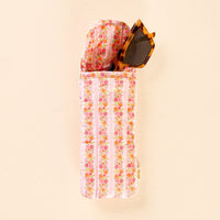 The Petal Parade Pink Sunglasses Case by the-darling-effect, featuring a floral pattern and quilted design with a magnetic flap closure, elegantly holds a pair of cat-eye tortoiseshell sunglasses—partially visible against a light beige background—for both essential protection and stylish flair.