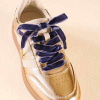 A gold sneaker with Velvet Blue Step It Up Shoelaces by The Darling Effect tied in a bow, adding a touch of luxury and flair.