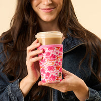 A woman in a denim jacket holds a drink wrapped in the-darling-effect’s Paradise Palms Sip Savvy Drink Sleeve.