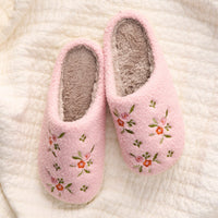 A pair of Dainty Floral Pink Fuzzy Slippers by the-darling-effect, featuring soft, fuzzy interiors and delicate floral embroidery in a cozy slip-on design, displayed on a cream-colored quilted fabric background.