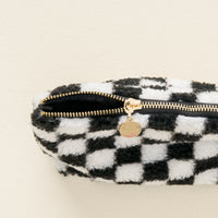 The Check Black Teddy Pouch by The Darling Effect is a fuzzy sherpa zippered pouch featuring a classic black and white checkerboard pattern and a gold zipper pull engraved with text, making it perfect for keeping your purse organized. Shown against a plain light background.