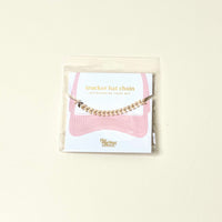 The Darling Effect's Gold-Leaf Chain Trucker Hat Chain, a chic hat accessory, comes on a white card with a pink hat illustration and "the tilting effect" text. Its shimmering gold chain stands out against the light background.