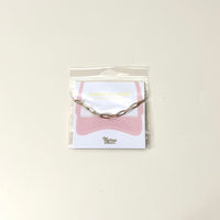 The Paperclip Chain-Gold Trucker Hat Chain by The Darling Effect is displayed on a branded card, making it the perfect accessory for your hat.