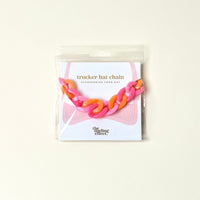 The Darling Effect’s Acrylic Sassy Trucker Hat Chain in pink and orange is a fun hat accessory, packaged on a white card with a pink hat illustration and “Accessorize your hat.”.