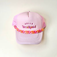 A pastel pink baseball cap with “HELLO weekend” embroidered in pink and red is styled with The Darling Effect’s Acrylic Sassy Trucker Hat Chain in chunky pink and orange, displayed on a plain white background.