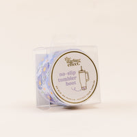 The Bouquet Beauty Purple Tumbler Silicone Boot by the-darling-effect comes in clear packaging labeled “no-slip tumbler boot,” with a cup and floral illustration, offering protection and helping to prevent tumbler dents.