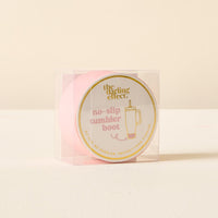 The Darling Effect Pink Tumbler Silicone Boot features gold trim and "the darling effect" text. This no-slip tumbler protector comes displayed in a clear plastic box.