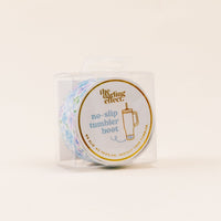 A clear plastic package contains the-darling-effect Secret Garden Blue Tumbler Silicone Boot, featuring a colorful pattern and gold-accented label with a cup illustration, designed to protect tumblers from dents.