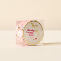 The Darling Effect’s Sweet Meadow Pink Tumbler Silicone Boot, featuring a floral design for maximum protection, is shown in a clear plastic box with a round front label against a softly lit off-white background.