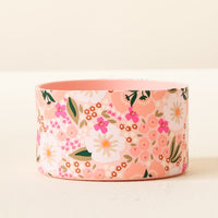 The Darling Effect Sweet Meadow Pink Tumbler Silicone Boot features a round, light pink floral design with white, pink, and peach flowers and green leaves, offering added tumbler protection with its no-slip grip.