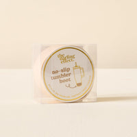 A clear plastic box holds The Darling Effect's Tan Tumbler Silicone Boot, a round, beige no-slip boot for tumbler protection. The cream label has a gold logo and simple tumbler illustration.
