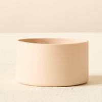 A simple, round, light beige ceramic bowl from The Darling Effect sits on a matching surface with its base wrapped in the Tan Tumbler Silicone Boot for added protection and stability against a neutral background.