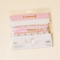 The-darling-effect’s Coquette Charm Tumbler Bracelet Stack features pink, white, and gold beaded charms in clear packaging with a pink and white label—perfect accessories for your 40 oz tumbler.