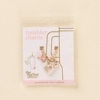 Add sparkle to your tumbler with the-darling-effect’s Glamour Tumbler Charm—featuring a gold chain, pink gem, pink bow, and white beaded heart! Packaged with "tumbler charm" and a cup graphic for stylish flair.