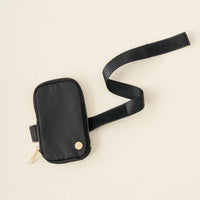 The Darling Effect Black Tumbler Fanny Pack is a small, water-resistant black pouch with a gold zipper and logo, attached to an adjustable Velcro strap—an elegant, stylish tumbler accessory shown on a light beige background.