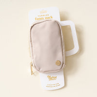 The Darling Effect's Natural Beige Tumbler Fanny Pack, featuring a gold zipper and round emblem, is shown on white packaging labeled “Tumbler Fanny Pack,” set against a cream-colored background.