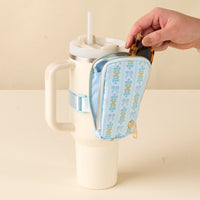 A hand puts sunglasses in the-darling-effect's Oh So Fancy Blue Tumbler Fanny Pack, which is attached to a cream travel mug with a straw.