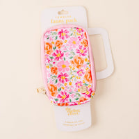 The Secret Garden Pink Tumbler Fanny Pack by the-darling-effect features a colorful floral pattern in pink, orange, and green, is water resistant, and includes a pink zipper with a gold pull. Displayed on white The Darling Effect packaging.