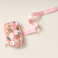 The Darling Effect's Sweet Meadow Orange Tan Tumbler Fanny Pack features a pink and orange floral pattern, gold zipper, light pink strap, and is water resistant—shown resting on a light-colored surface.