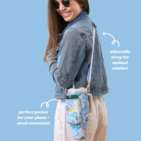 A woman smiles while wearing a denim jacket and linen pants, carrying The Darling Effect’s Beyond Blooms Blue Green Tumbler Sling with a phone pocket and adjustable strap.