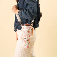 A person carries the-darling-effect's Endless Daydream Cream Tumbler Sling, featuring an adjustable strap, over their shoulder for a hands-free experience while wearing a denim jacket and white pants.