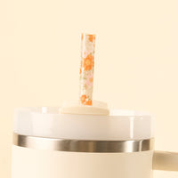 The the-darling-effect Bouquet Beauty Sage 40 oz Tumbler Straw Set features a BPA-free reusable straw with an orange floral pattern, standing upright in the lid of a white insulated tumbler against a cream background.