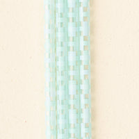 Close-up of The Darling Effect's Check Blue 40 oz Tumbler Straw Set, featuring several rows of translucent blue square straws arranged in a woven pattern against a pale, textured background.