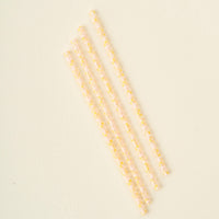 The Darling Effect’s Check Peach 40 oz Tumbler Straw Set features four clear, reusable eco-friendly straws with a yellow and white checkered pattern, arranged diagonally on a plain, light-colored surface.