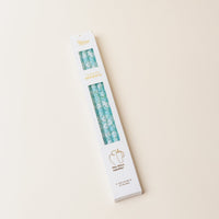 A white rectangular box of The Darling Effect Daisy Craze Aqua 40 oz Tumbler Straw Set with a blue and white pattern, gold and yellow lettering, and a small cup illustration is shown on a light beige background.