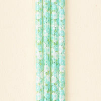 Four aqua reusable straws with a white and green daisy design from The Darling Effect’s Daisy Craze Aqua 40 oz Tumbler Straw Set are arranged vertically on a cream background—ideal eco-friendly accessories for your 40 oz tumbler.