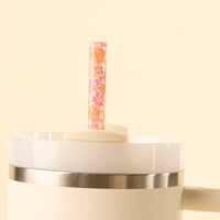 A close-up of the-darling-effect’s Secret Garden Pink 40 oz Tumbler Straw Set, featuring a white cup with a silver band and floral-patterned reusable straw, against a light beige background.