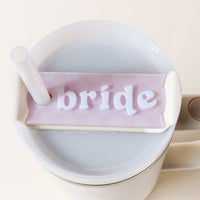 The Darling Effect's Bride Tumbler Lid Tag is a pastel pink acrylic name plate reading "bride" in white—perfect for personalizing your cup with a straw and adding charm to special occasions.