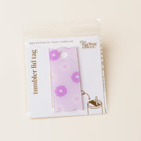 The Darling Effect's Darling Daisy Purple Tumbler Lid Tag features pink and purple flowers on a light purple background. Packaged with “tumbler lid tag” and “The Darling Effect” text plus a tumbler cup illustration—ideal for customizing lids.